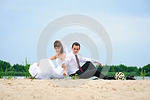 Loving wedding couple sitting near water and strew sands