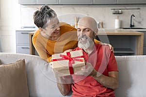 Loving wife surprising her mature husband with gift at home