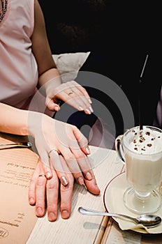 Loving woman hold man hand in her hands. Just married couple showing up wedding rings. Near Cup of latte coffee with chocolate on