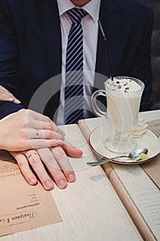 Loving woman hold man hand. Just married couple showing up wedding rings. Near Cup of latte coffee with chocolate in cafe