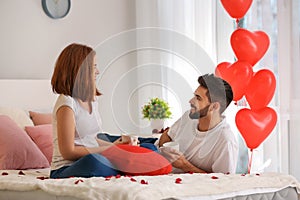 Loving young couple drinking coffee on bed at home. Celebration of Saint Valentine's Day