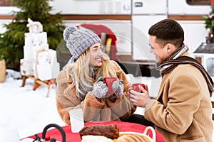 Loving Young Couple Drinking Hot Chocolate While Sitting Outdoors At Winter Campsite