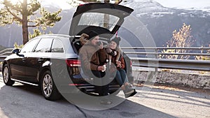 Loving, young couple drinks hot tea from thermos flask sitting in car trunk. Happy caucasian couple having a coffee