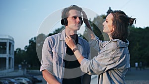 Loving young couple in evening soft sunlight. The girl puts her headphones on her boyfriend`s head and kissing him. Park