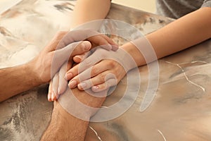 Loving young couple holding hands on color table, closeup