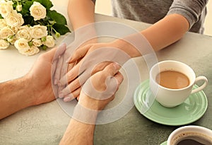 Loving young couple holding hands on light table, closeup