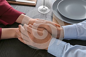 Loving young couple holding hands on wooden table, closeup