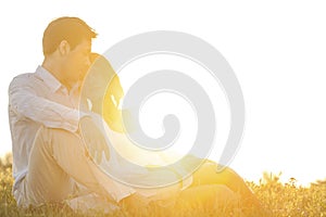 Loving young couple sitting on grass at park against clear sky