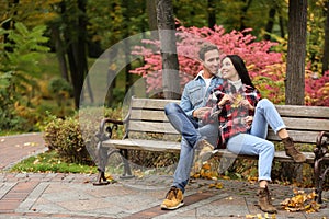 Loving young couple sitting on wooden bench in autumn park