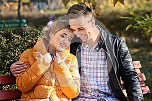 Loving young couple sitting on wooden bench in autumn park