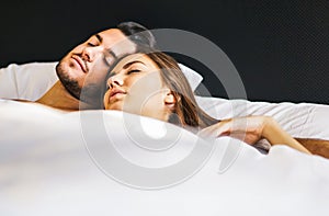 Loving young couple sleeping together in a bed with white sheets at home - Life`s moments of people in love in the bedroom