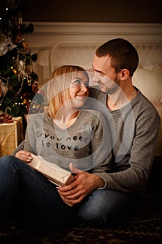 Loving young couple spends Christmas at home near a decorated, festive Christmas tree. Man and woman are happy spending