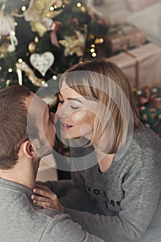 Loving young couple spends Christmas at home near a decorated, festive Christmas tree. Man and woman are happy spending