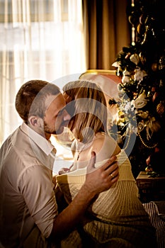 Loving young couple spends Christmas at home near a decorated, festive Christmas tree. Man and woman are happy spending