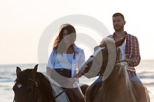 a loving young couple in summer clothes riding a horse on a sandy beach at sunset. Sea and sunset in the background