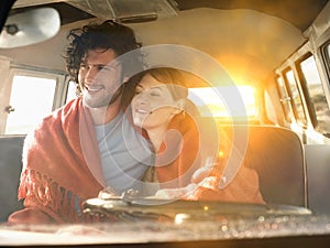 Loving young couple wrapped with blanket in front seat of campervan