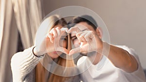 Loving young family of two making heart with their fingers at home, focus on hands
