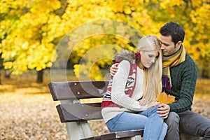 Loving young man hugging shy woman on park bench during autumn