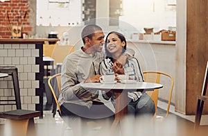 Loving young man sitting with his arm around his girlfriend while sitting at a table and having coffee in a cafe. Loving