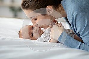 Loving Young Mom Kissing Her Cute Newborn Child While Relaxing In Bed