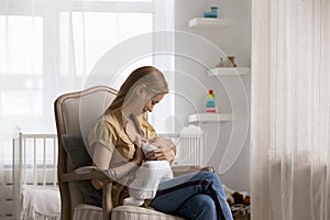 Loving young mother breastfeeding baby, sitting in armchair at home