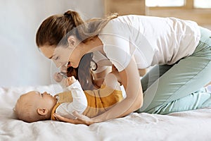Loving young mother caressing her cute baby boy at bedroom