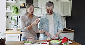 Loving young woman feeding smiling husband, preparing food together.