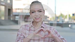 Loving Young Woman showing Heart Shape by Hands Outdoor