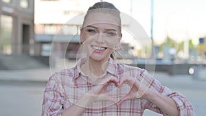 Loving Young Woman showing Heart Shape by Hands Outdoor