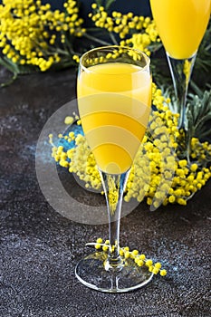 Low alcohol cocktail mimosa with orange juice and cold dry champagne or sparkling wine in glasses, blue background with flowers,