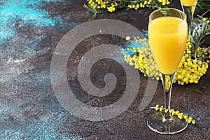 Low alcohol cocktail mimosa with orange juice and cold dry champagne or sparkling wine in glasses, blue background with flowers,