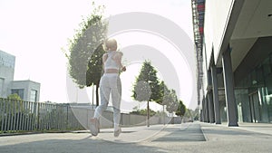 LOW ANGLE Active young woman jogging past modern building and avenue on warm day