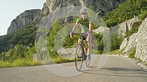 LOW ANGLE: Athletic man riding his road bicycle down the empty asphalt road.