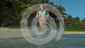 LOW ANGLE: Attractive female tourist runs in the sea and splashes water around