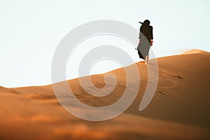 Low angle beautiful woman in long black dress barefoot walk up follow walk on golden Sahara desert dunes