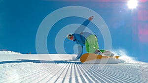 LOW ANGLE: Cheerful young male snowboarder carving a freshly groomed slope.