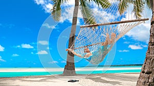 LOW ANGLE: Cheerful young woman relaxing under the palms in the comfy hammock.