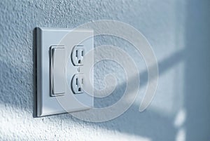 Close-Up Of Modern White Light Switch And Electrical Outlet On Textured Wall