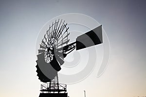 Low angle close up of isolated antique metal silhouette wind wheel turbine on steel tower against gray dawn cloudless sky near