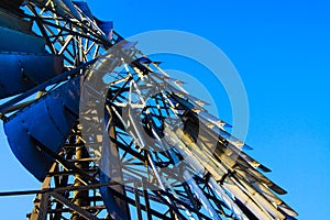 Low angle close up of isolated antique metal wind wheel turbine on steel tower against blue cloudless sky near Zaanse Schans,