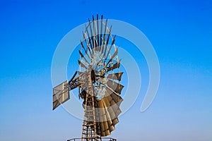 Low angle close up of isolated antique metal wind wheel turbine on steel tower against blue cloudless sky near Zaanse Schans,