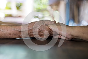 Low angle close-up shot of two wrinkled hands of two elderly Thai women holding each other in consolation