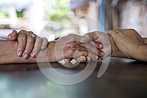 Low angle close-up shot of two wrinkled hands of two elderly Thai women holding each other in consolation