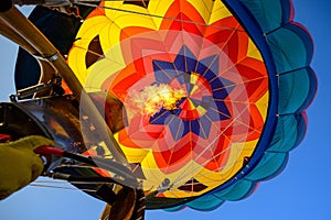 Low angle of a colorful hot air balloon and flames coming out of its burner against the blue sky