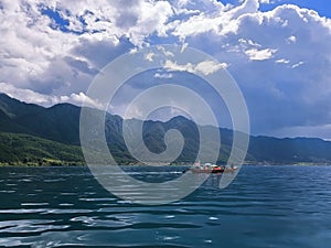Low-angle of Como lake sunlit forested mountains and cloudy sky background