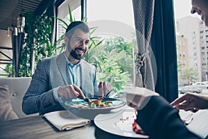 low angle cropped photo of a brunet guy stting in a fancy restaurant`s terrace with view, in a formalwear and smiling, looking