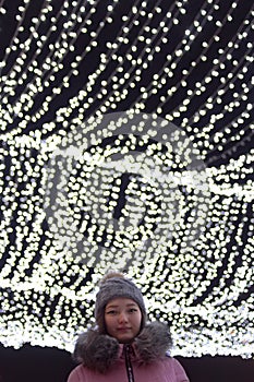 Low angle headshot of woman with christmas lights on background, sky festive illumination shine and glow, urban holiday