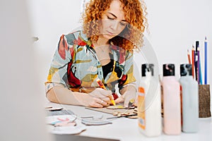 Low angle image of a woman sitting behind desk, painting wooden shapes.