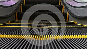 Low angle looped perspective view of modern escalator stairs. Automated elevator mechanism. Yellow line on stairway illuminated