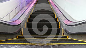 Low angle looped perspective view of modern escalator stairs. Automated elevator mechanism. Yellow line on stairway illuminated